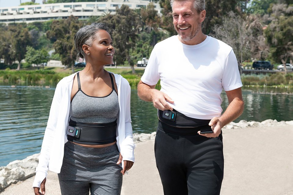 A man and a woman walking outdoors wearing a smart toning belt.